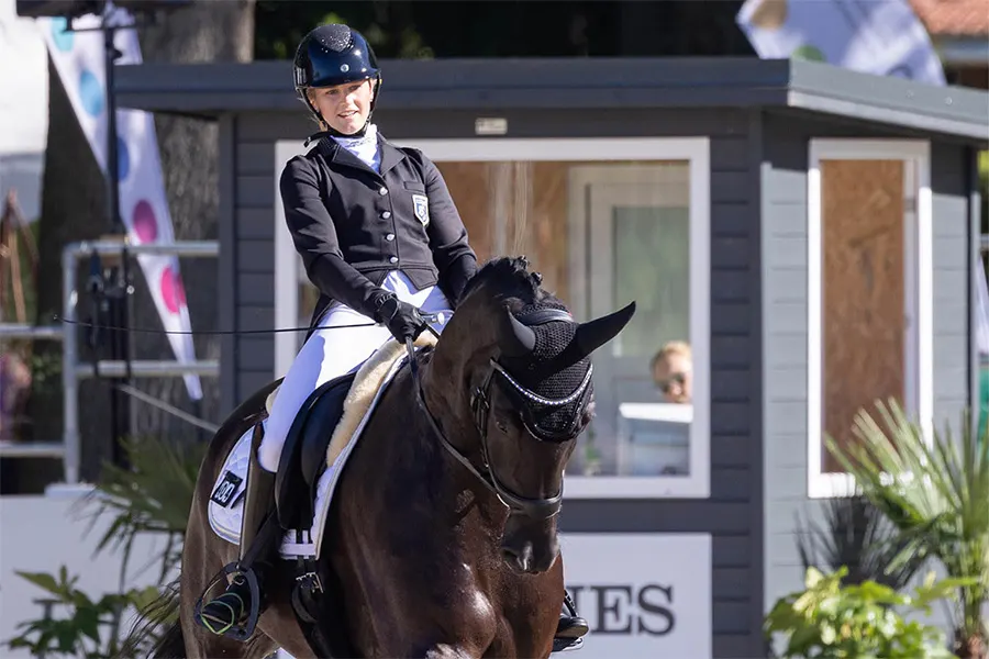 Laura Kangasniemi ratsastamassa tummanruskealla ratsullaan kouluratsastuskisavarustuksessa.